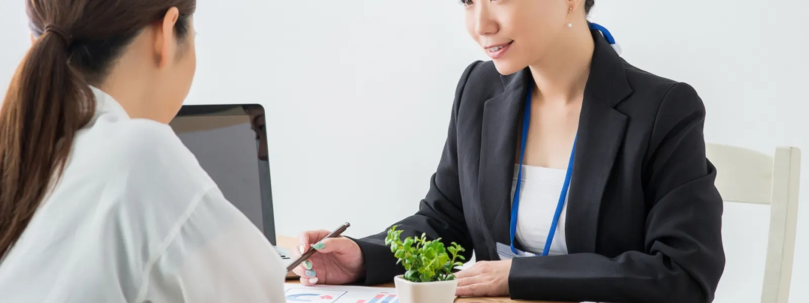 スーツを着た女性が私服の女性にペンを持って説明している様子