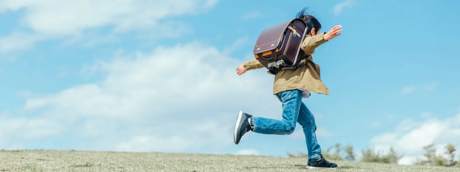 ランドセルを背負った小学生が芝生の上を走っている様子