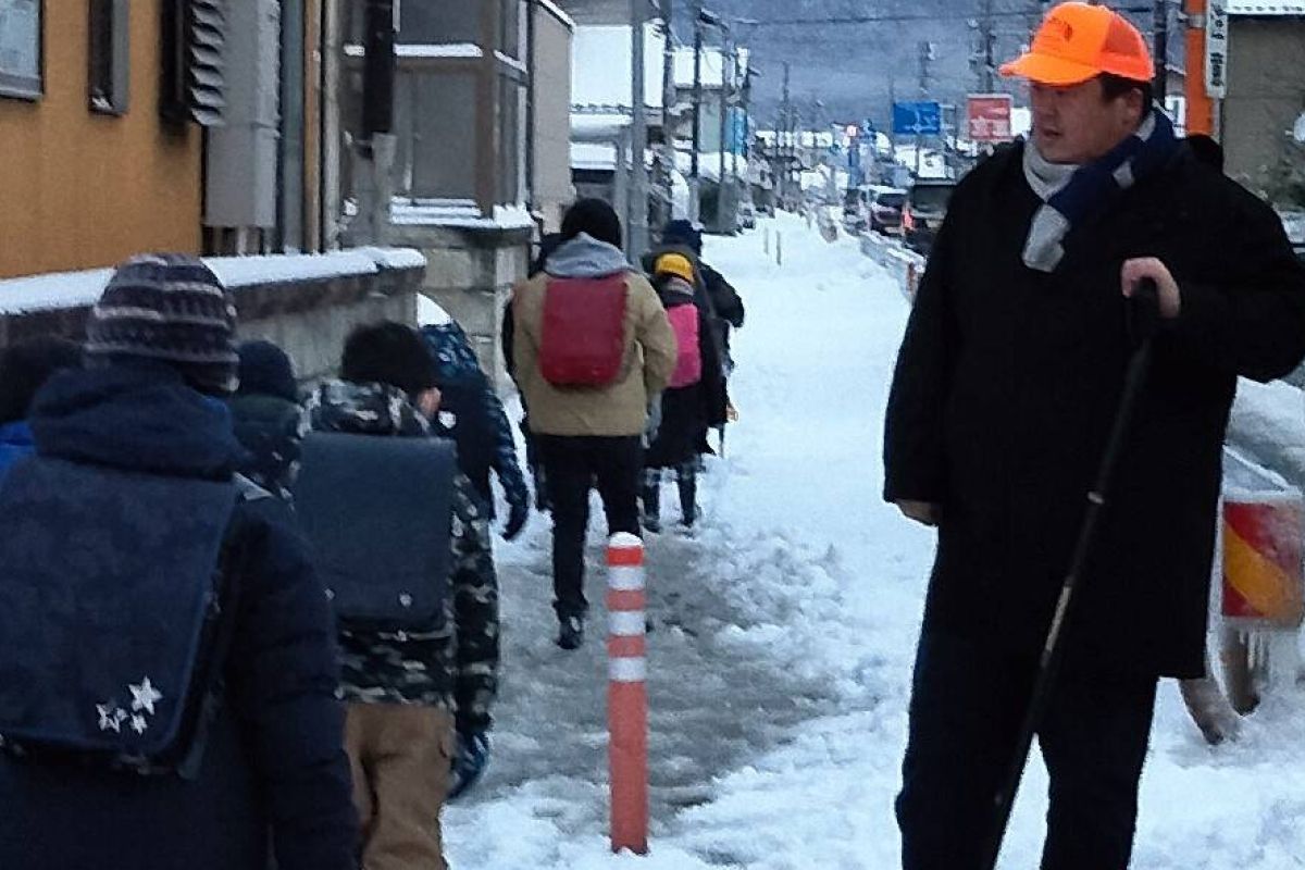 雪道の通学路で雪かきをしながら子どもたちを見送る幸田健太
